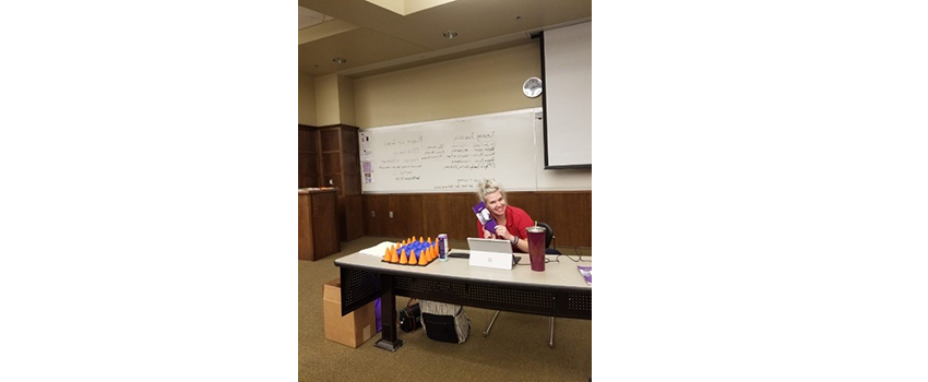 Person sitting at desk smiling with whiteboard behind her.